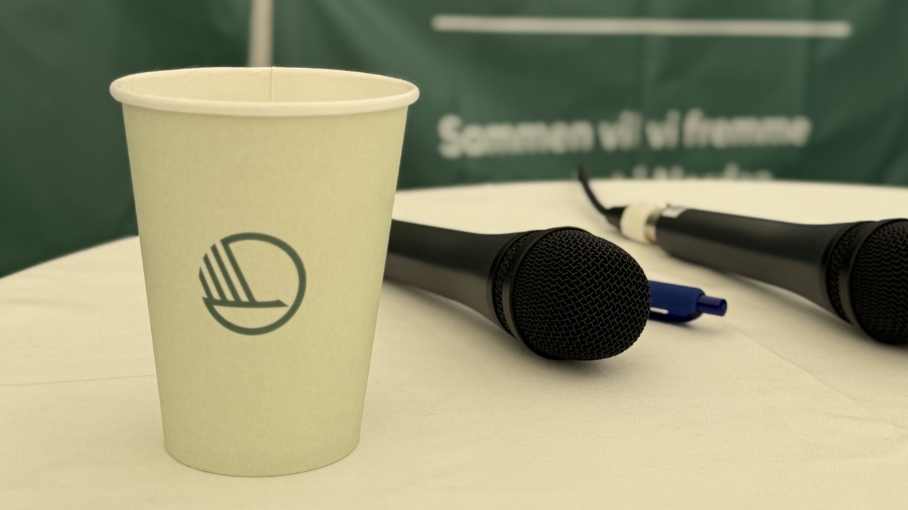 Paper cup with the Nordic swan log standing next to a microphone laying on the table