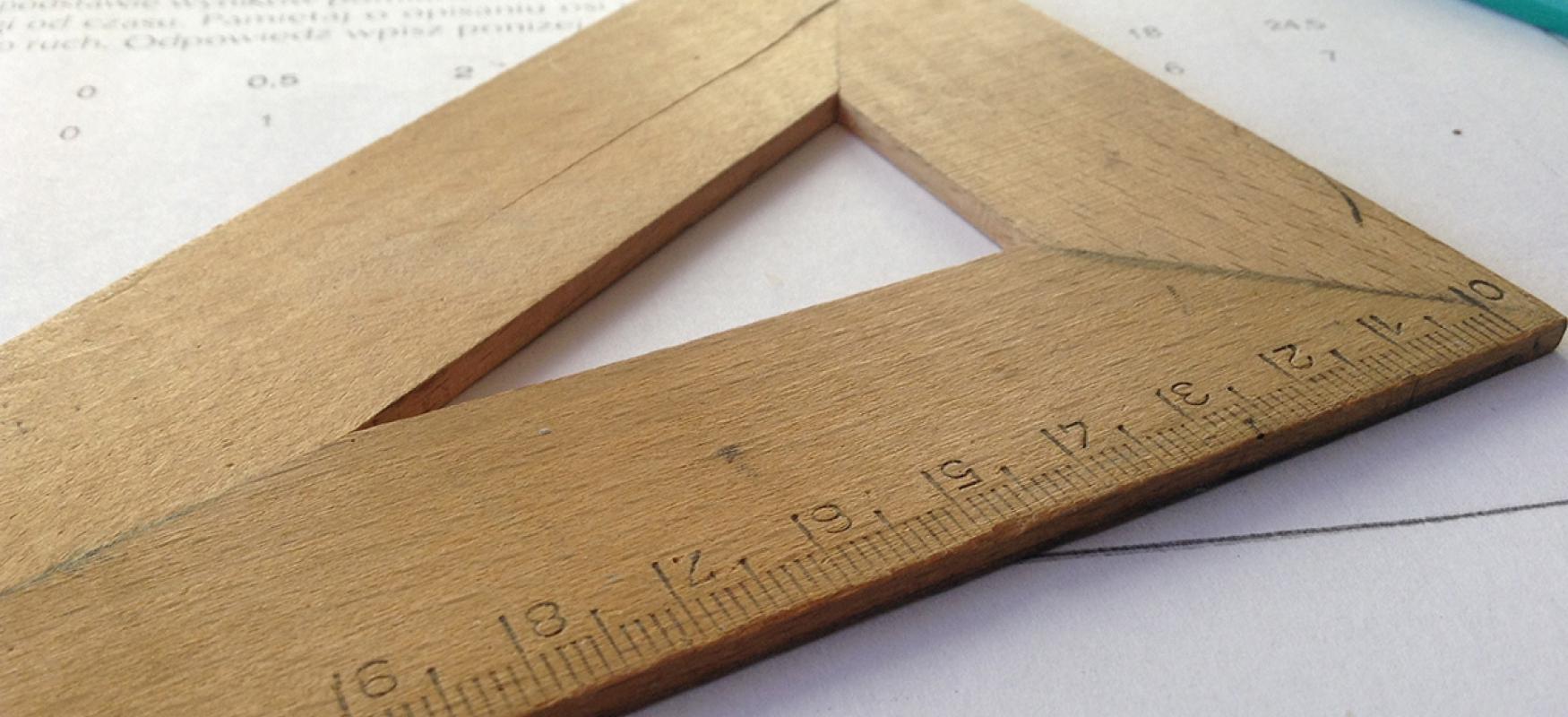 A wooden triangle ruler lying on top of handwritten notes.