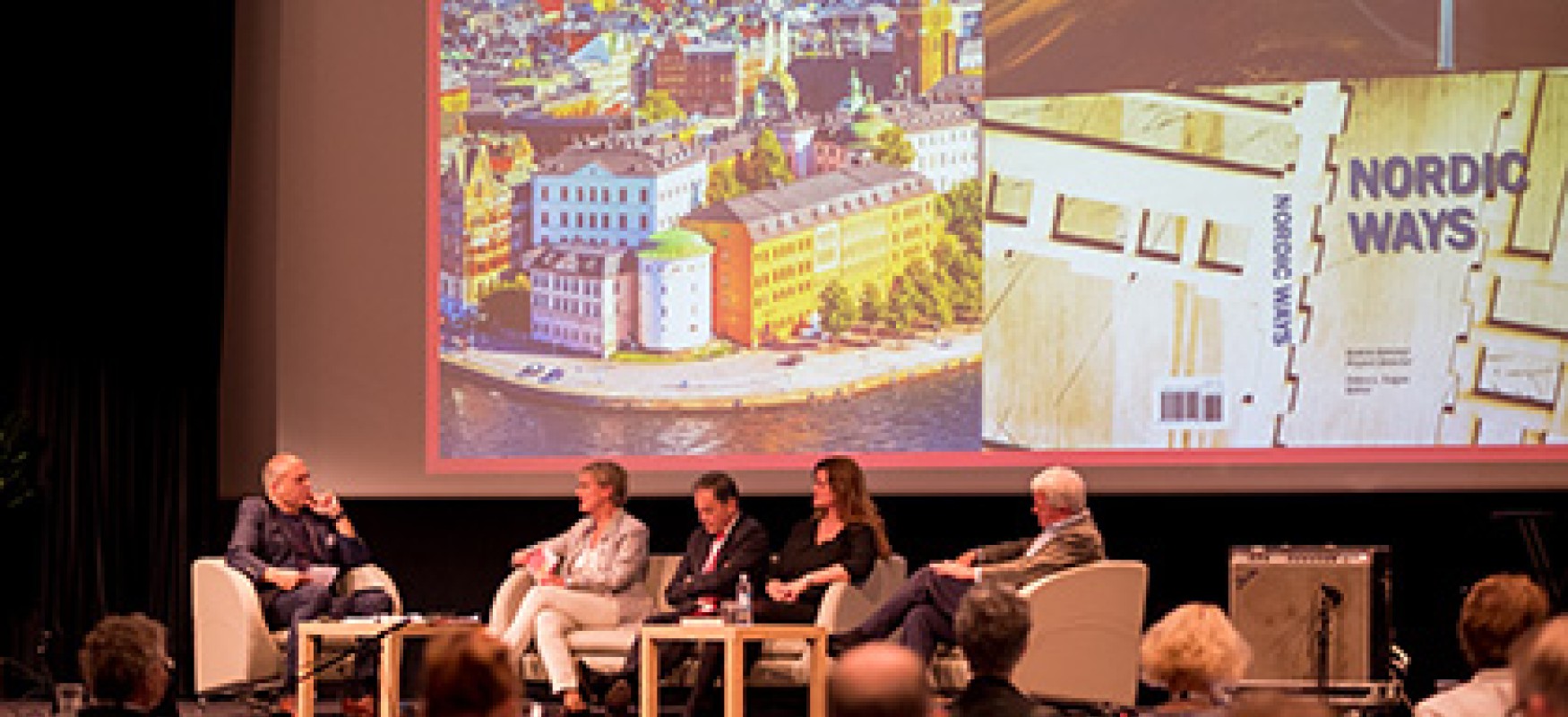 People sitting on stage in front of a presentation screen.