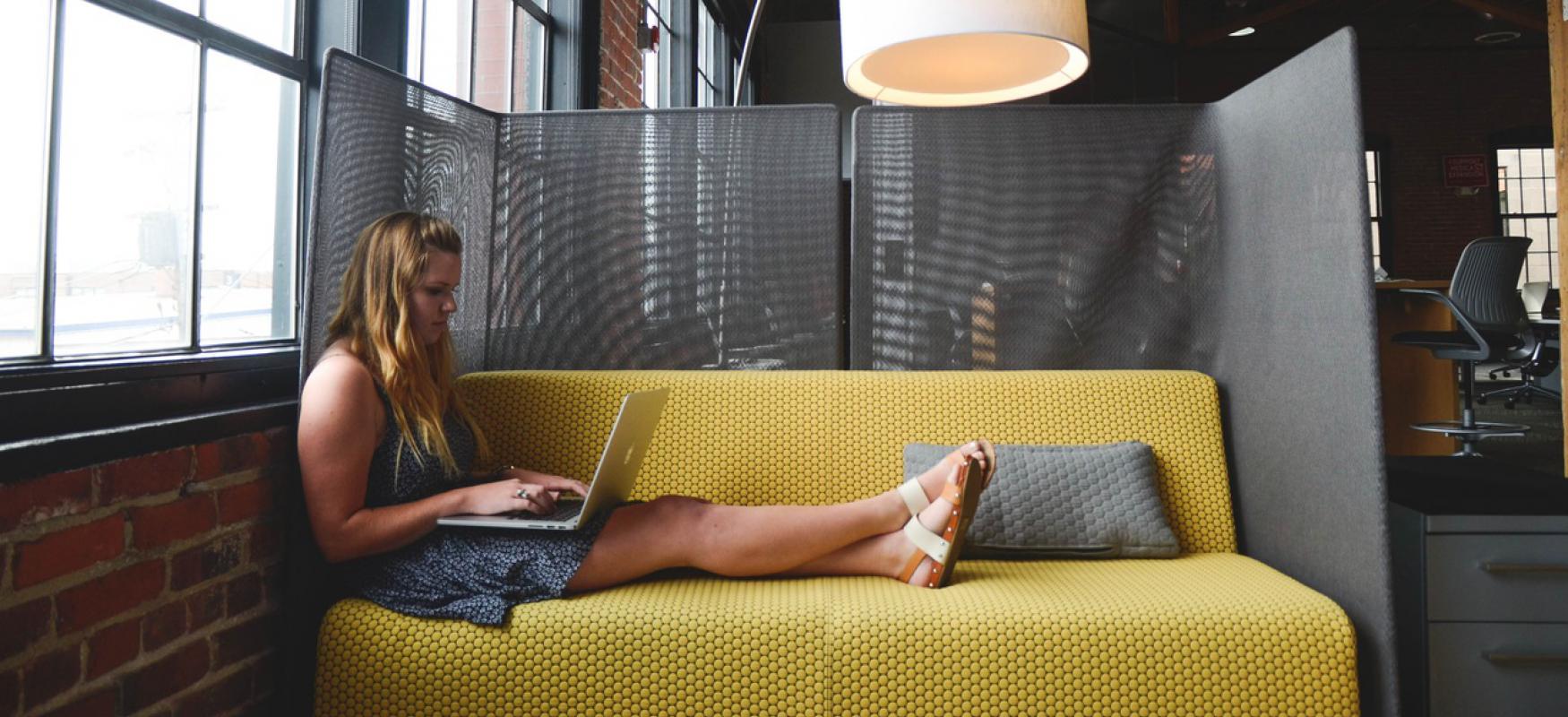 Woman sitting in a sofa with a computer and working. Large lamp hanging over the sofa.