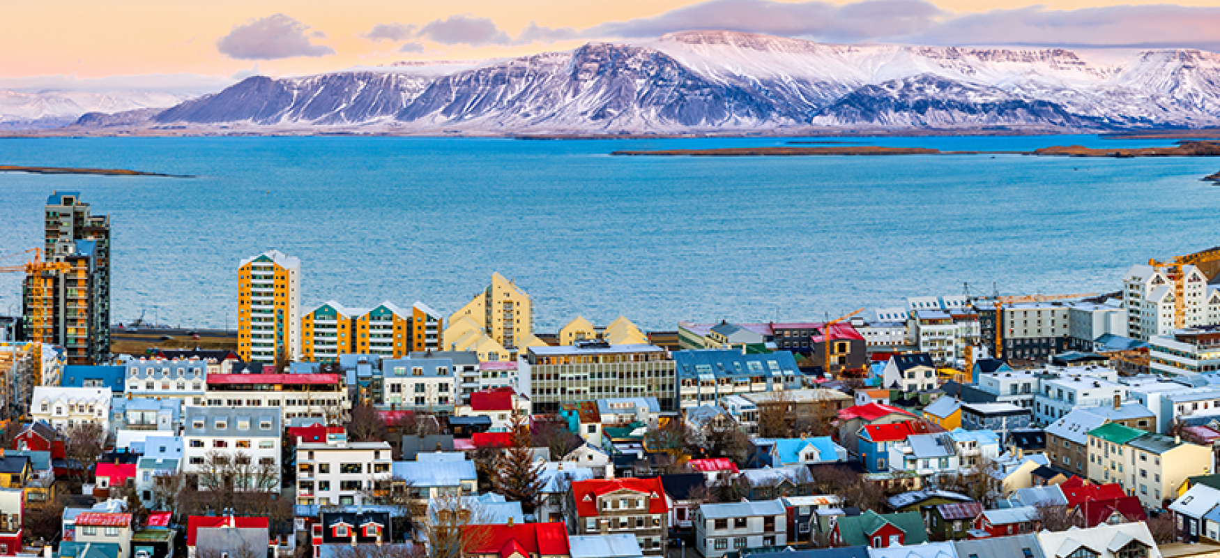 Aerial panorama of downtown Reykjavik at sunset with colorful houses and snowy mountains in the background