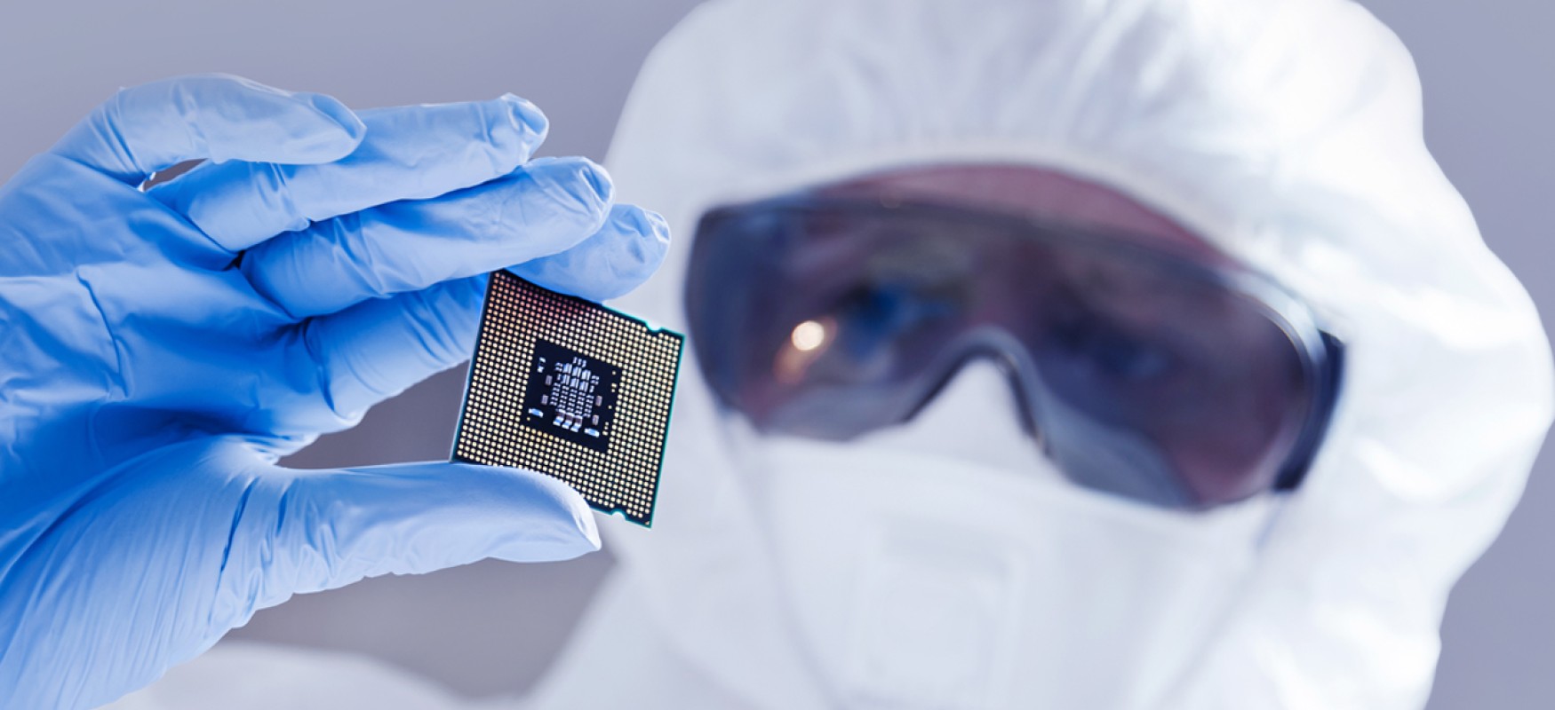 Person wearing lab gear holding up a semiconductor chip