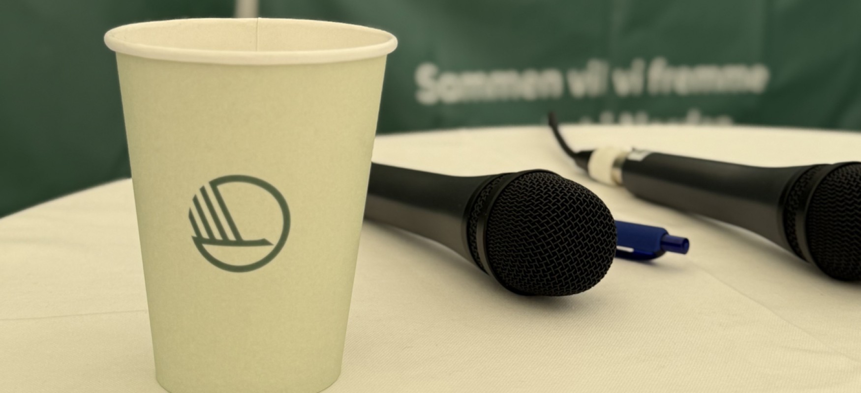 Paper cup with the Nordic swan log standing next to a microphone laying on the table