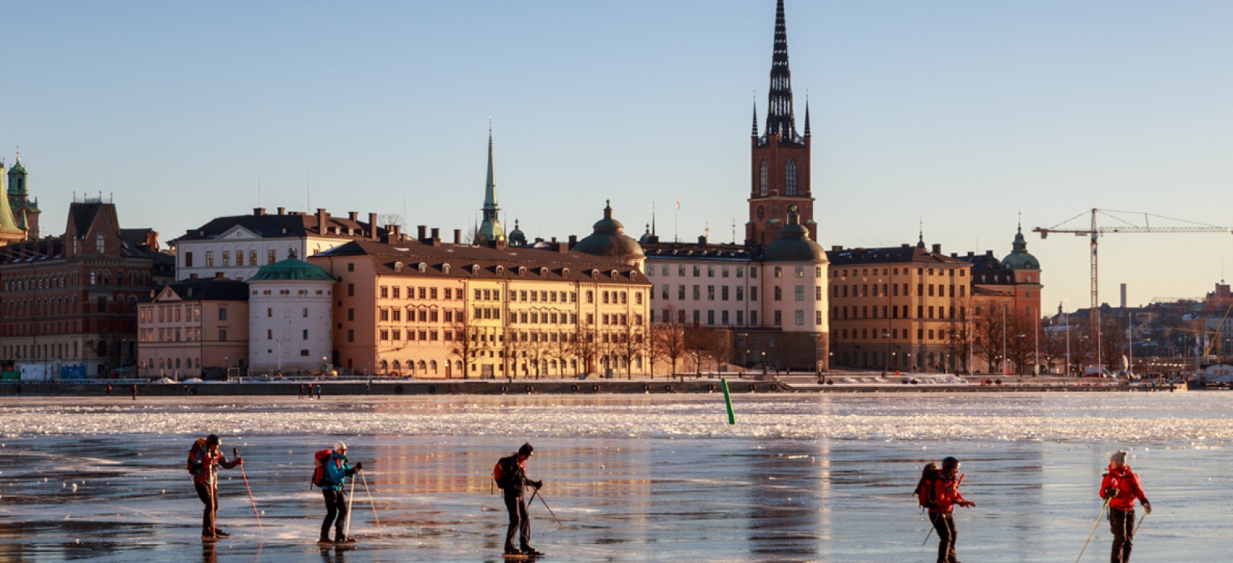 Five person ice skating frozen Riddarfjärden bay by Gamla Stan island, on a sunny winter day in Stockholm