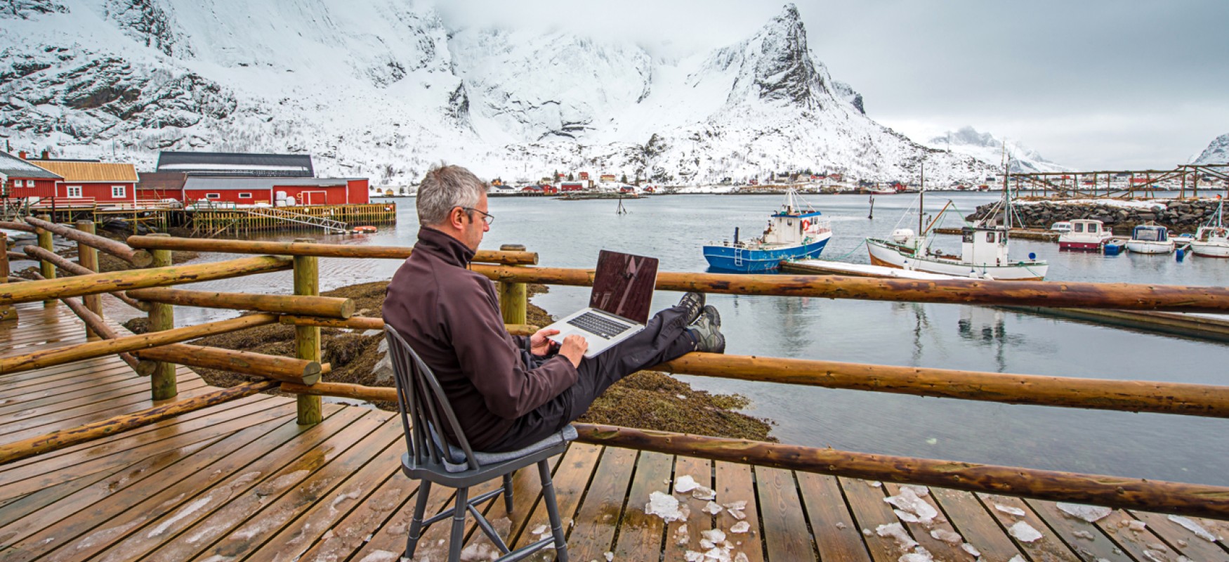 Man sitting on a chair on the dock in Lofoten working on a computer