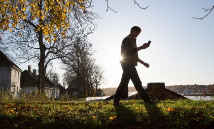 Man walking in the grass in an urban setting, looking at his phone.