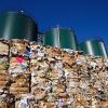 Piles of compressed trash in front of three silos.