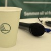 Paper cup with the Nordic swan log standing next to a microphone laying on the table